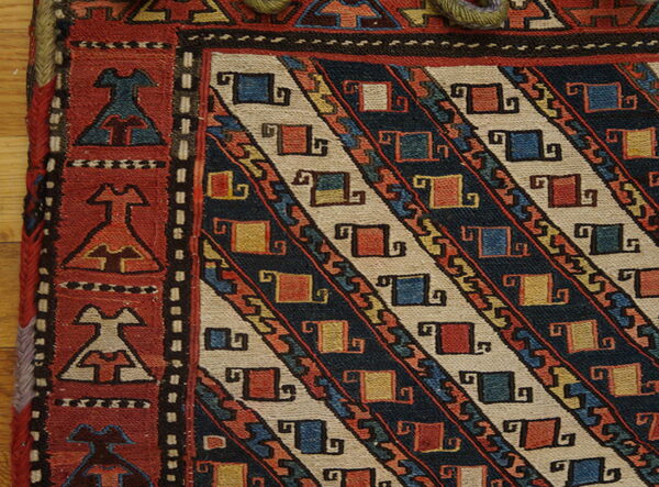 Detailed view of a flatweave rug with a red border and a field of navy and beige diagonal geometric stripes.