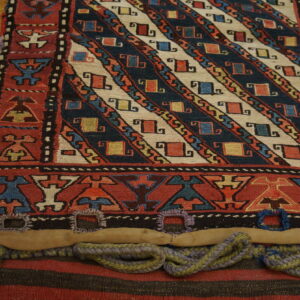 Detailed view of a woven textile featuring diagonal navy and cream stripes and red geometric borders on wood.