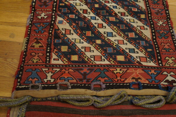 Detailed view of a woven textile featuring diagonal navy and cream stripes and red geometric borders on wood.