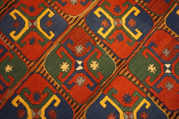 Detail of a flatweave rug with large diamonds in red, blue, green, and yellow geometric patterns.