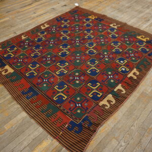 A colorful flatwoven rug with a geometric grid pattern in red, blue, green, and yellow on distressed wooden floorboards.