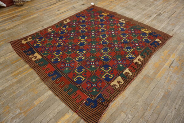 A colorful flatwoven rug with a geometric grid pattern in red, blue, green, and yellow on distressed wooden floorboards.