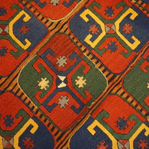 Low-pile rug detail showing a repeating red, blue, green, and yellow geometric lattice pattern.