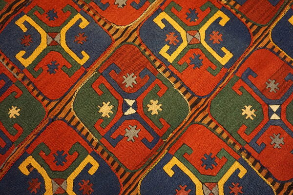 Low-pile rug detail showing a repeating red, blue, green, and yellow geometric lattice pattern.