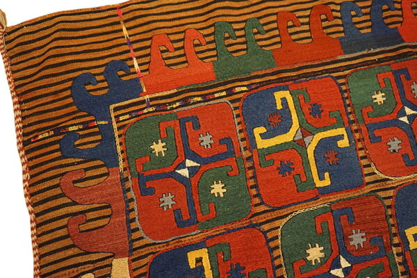 Flatweave rug detail showing red, blue, and green geometric motifs bordered by tan and black horizontal stripes.