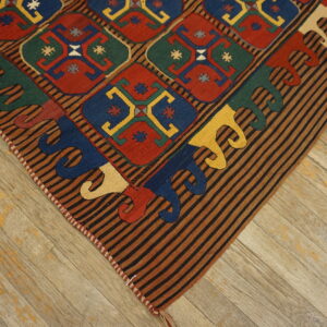 Low-pile rug corner with multi-colored geometric diamonds and a striped border on distressed wood flooring.