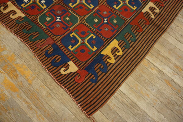 Low-pile rug corner with multi-colored geometric diamonds and a striped border on distressed wood flooring.
