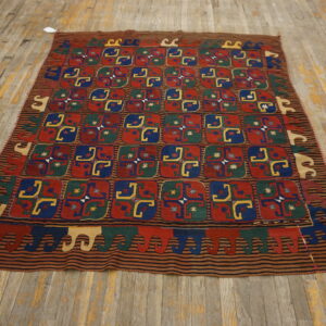 Geometric kilim rug in red, blue, green, and yellow displayed on light, worn hardwood flooring.