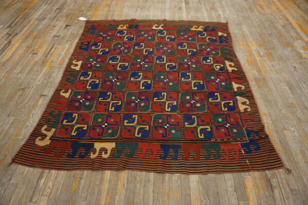 Geometric kilim rug in red, blue, green, and yellow displayed on light, worn hardwood flooring.