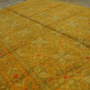 A textured, gold-colored shag rug with orange and red abstract patterns is laid over gray wood planks.