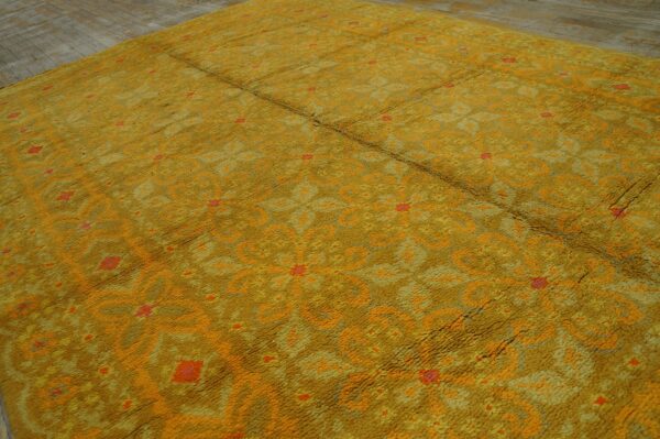 A textured, gold-colored shag rug with orange and red abstract patterns is laid over gray wood planks.