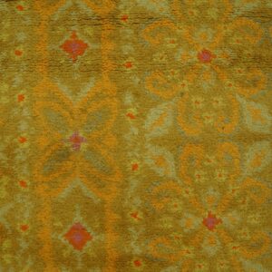 Textured, golden yellow rug with orange and pink abstract patterns next to wooden flooring.