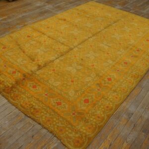 Shaggy gold and olive rug featuring a geometric pattern with coral accents on worn wood floors.