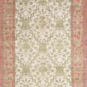 A low-pile rug displaying repeating green urns on cream, framed by an elaborate rose and green border.