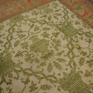 A beige rug with a green vine pattern and a wide coral border rests on wood flooring.