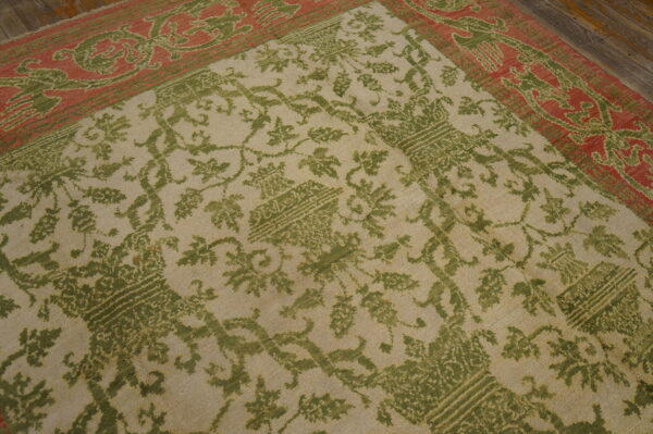 A beige rug with a green vine pattern and a wide coral border rests on wood flooring.