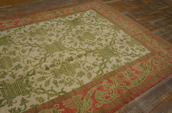 Beige rug with a green floral pattern and a wide red border on rustic wooden floorboards.