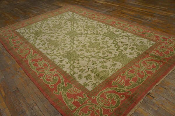 Beige rug with olive green foliage motifs and a contrasting terra cotta border on dark plank flooring.