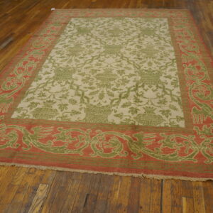 A low-pile rug with a cream field, green vine pattern, and a coral-and-green ornate border on wood flooring.