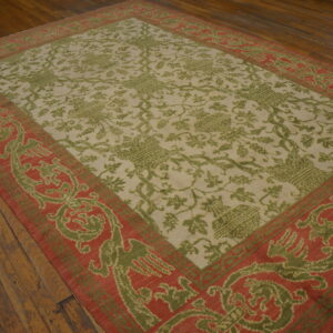 Olive green and cream patterned rug with a wide red-orange border is laid on dark wood floors.