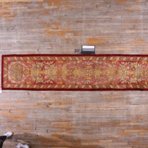 Runner rug with a reddish border and pale pink floral pattern displayed on bleached wood flooring.