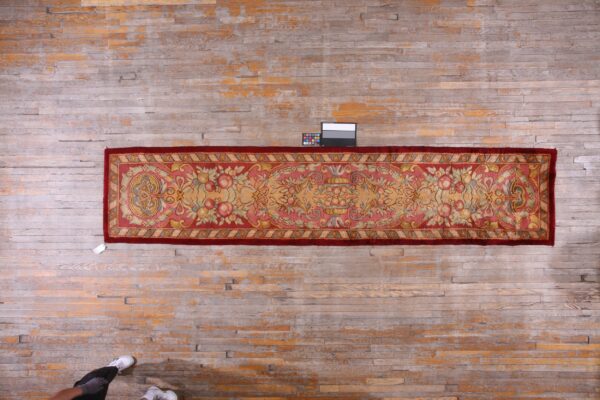 Runner rug with a reddish border and pale pink floral pattern displayed on bleached wood flooring.