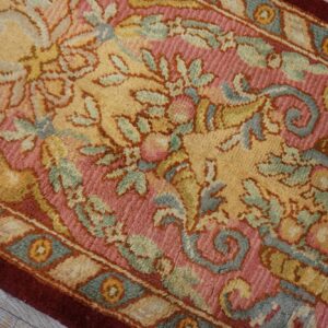 Detailed close-up of a rose, gold, and teal ornate floral runner on gray wood flooring.
