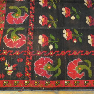 Dark rug with bright red, green, and cream folk floral motifs and geometric borders on wood floors.