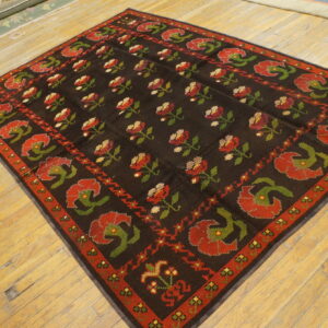 Dark brown rug patterned with repeating red and green floral designs sits on light hardwood flooring.