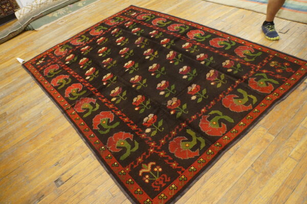 Dark brown rug patterned with repeating red and green floral designs sits on light hardwood flooring.