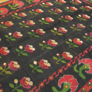 Black rug with repeating rows of cross-stitch style red, green, and magenta floral patterns.
