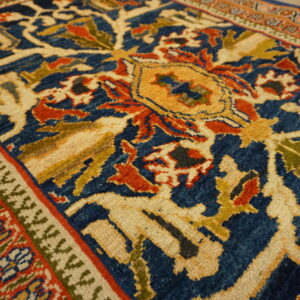 Traditional rug detail showing blue, red, and gold floral patterns, heavy border, and wood plank flooring.