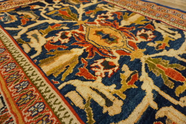Traditional rug detail showing blue, red, and gold floral patterns, heavy border, and wood plank flooring.