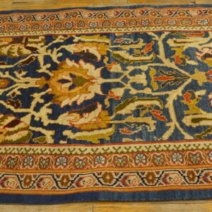 Ornate runner with dark blue field and gold, red, and green complex floral patterns on wood flooring.
