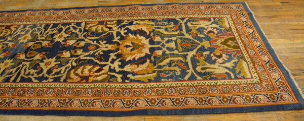 Ornate runner with dark blue field and gold, red, and green complex floral patterns on wood flooring.