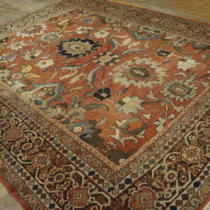 Ornate low-pile rug featuring a rust and multicolored floral pattern with complex borders on wood flooring.