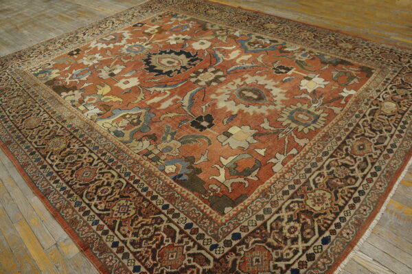 Ornate low-pile rug featuring a rust and multicolored floral pattern with complex borders on wood flooring.