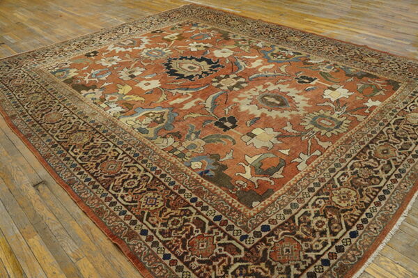 Ornate traditional rug with a terracotta field and detailed borders rests on worn wooden floorboards.