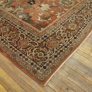 Rust colored rug corner with intricate brown and beige border on light, weathered wood floorboards.