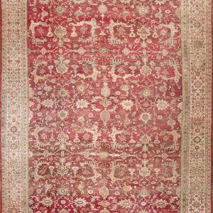 Full view of a red rug featuring distressed ornate floral and vine motifs with a wide beige border.