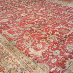Low-pile distressed red rug featuring complex beige and pale blue traditional floral and vine patterns.