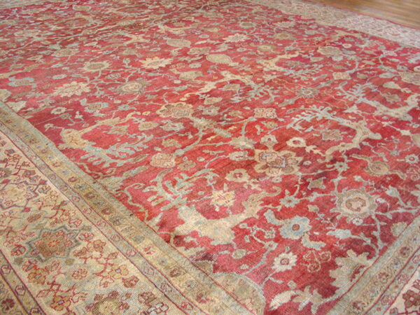 Low-pile distressed red rug featuring complex beige and pale blue traditional floral and vine patterns.