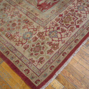 Ornate beige rug with deep red and pale blue floral borders resting on rustic wood plank flooring.