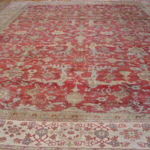 Low-pile red rug with an ornate beige and blue floral design on a wooden floor.