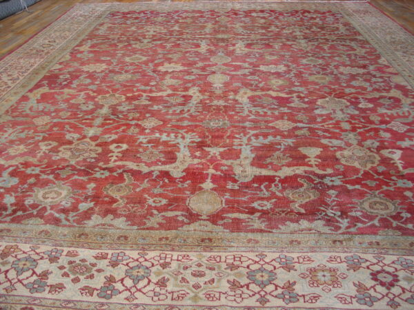 Low-pile red rug with an ornate beige and blue floral design on a wooden floor.
