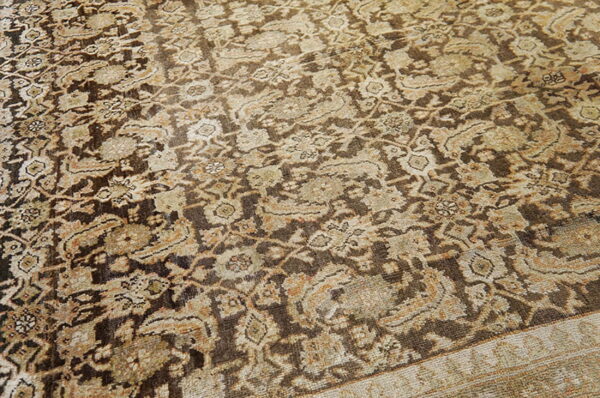 Distressed rug featuring a dense traditional pattern in earthy dark brown, tan, and faded cream colors.