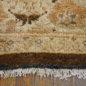 Close-up of a textured beige and brown rug with wide dark borders and white fringe on wood flooring.
