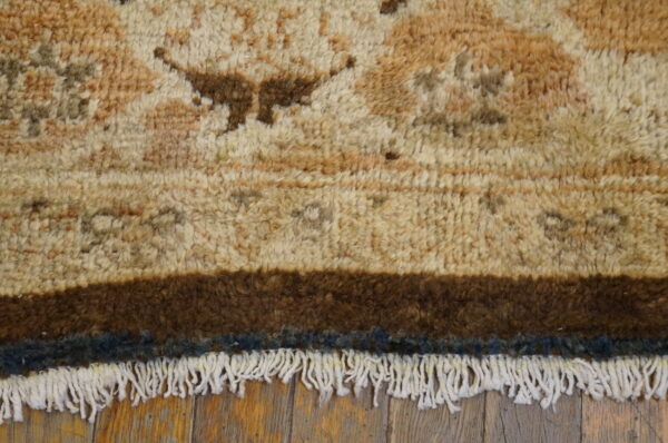 Close-up of a textured beige and brown rug with wide dark borders and white fringe on wood flooring.