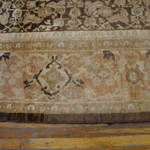Ornate traditional rug border in shades of beige, brown, and pale rose on hardwood floors.