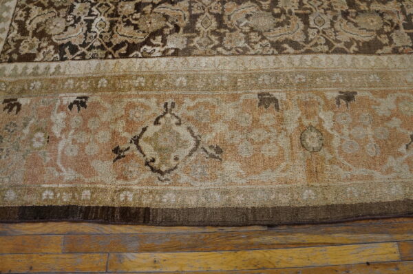 Ornate traditional rug border in shades of beige, brown, and pale rose on hardwood floors.